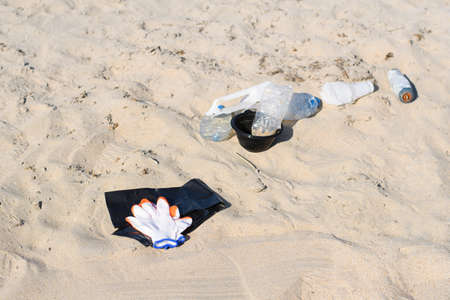 Gloves with a trash bag lie on the sandy beach against the background of trash. The concept of...