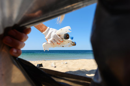 Garbage collection from the beach close-up. View from the trash bag. Selective focus on hands with debris.の写真素材