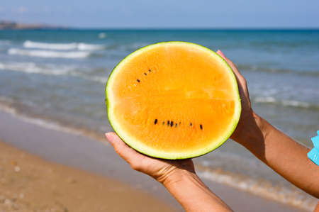 Orange watermelon in hands on the background of the sea. A unique variety of watermelon.の写真素材