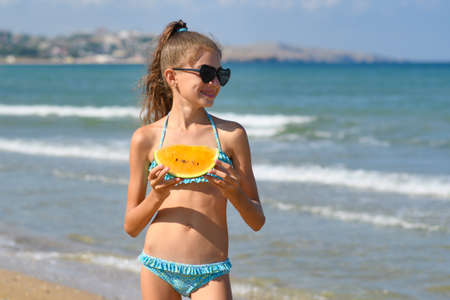 A happy girl stands on the seashore with a slice of watermelon and looks at the sea.の写真素材