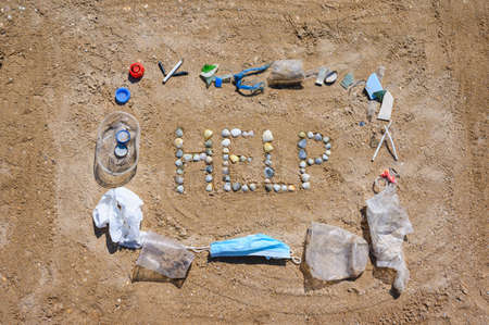 Nature asks for help from pollution. The word HELP from small seashells in the sand. Garbage is spread around.の写真素材