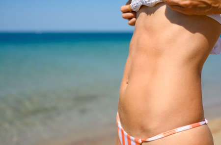 Slender flat belly of a girl on the background of the sea on a sunny day. The result of a healthy...