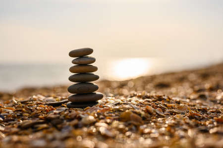 Black pebble pyramid on a seashell beach at sunset. Calm scene and privacy. Selective focus, narrow focus.の写真素材