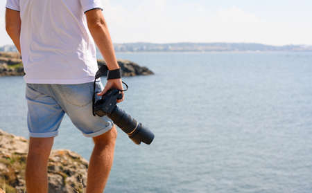 A photographer with a large camera close-up on the background of the sea stands on the top of the mountain. Unrecognizable person.の写真素材