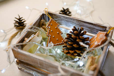 Home preparation for Christmas. Wooden box with New Year's toys, pine cones and a garland. Selective focus on a toy in the shape of a Christmas tree and gingerbread cookie.の写真素材