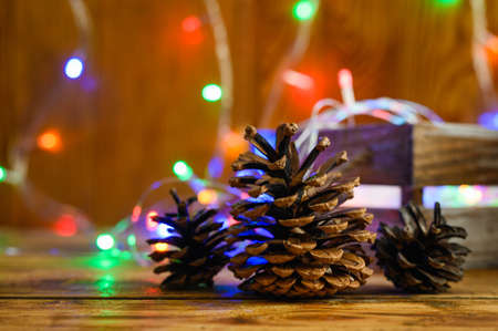 Greeting Christmas card with fir-tree cones and Christmas lights on a wooden background. Selective...