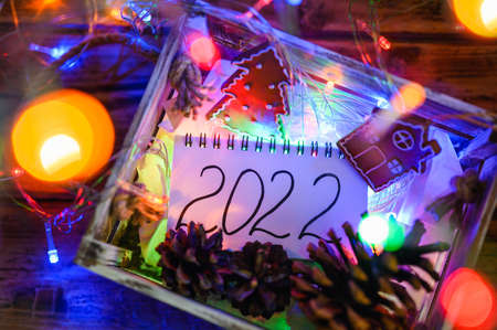A small notebook with the inscription 2022 lies in a wooden box with pine cones, toys and colorful...