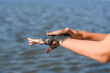 Close-up of a hand brush smearing with black curative mud from a salt lake. Treating arthritis of the joints of the hands with natural remedies. Selective focusing.の写真素材