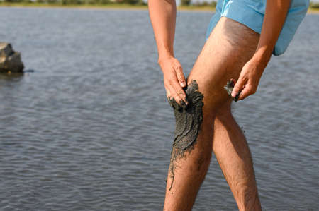 The man of the lake smears his knee with black medicinal mud from salty. Alternative medicine for the treatment of joints. Selective focusing.の写真素材