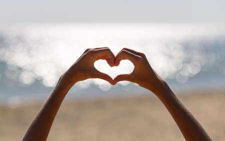 Children's hands gesture in the shape of a heart on the background of sun glare of the sea....