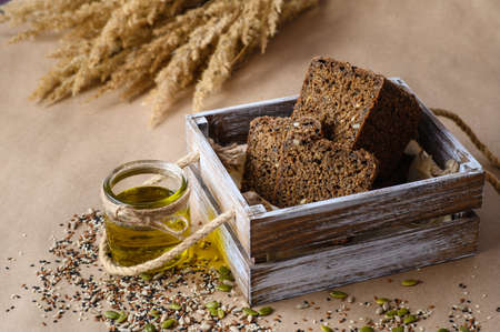 Vintage wooden box with dark rye bread. There are many seeds and a jar of olive oil nearby.の写真素材
