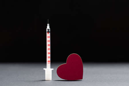 Insulin syringe and red heart stand on a black background. Diabetes protection conceptの写真素材