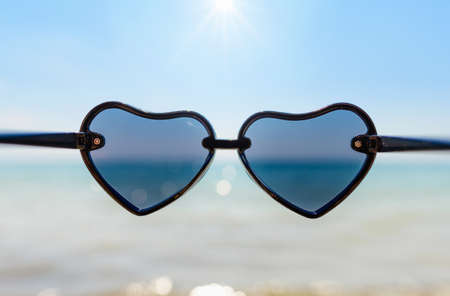 Sunglasses in the shape of a heart on the background of the sea and blue sky with the sun. Relaxation vacation concept by the seaの写真素材
