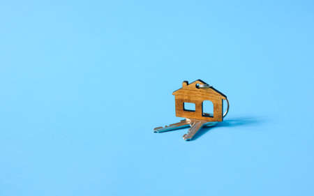 Small figurine of a house with keys to the lock on a blue background. The concept of buying your own home.の写真素材