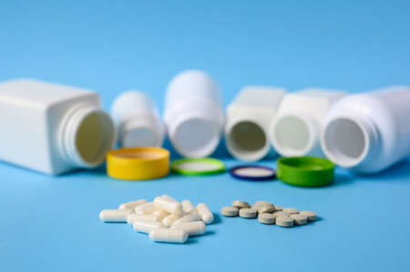Pills on a blue background and a lot of empty open drug cans. Selective focus on tablets.