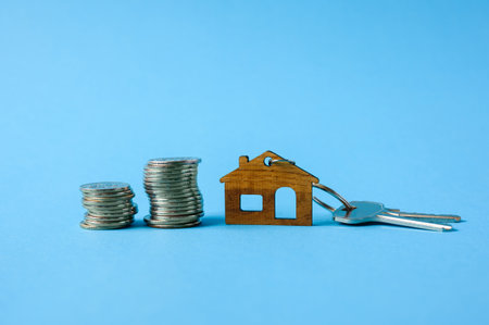 Coins, keys and a small wooden house on a blue background. New home buying conceptの写真素材