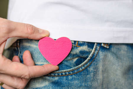 Close-up of a man pulls a small pink heart out of his pocket. Selective focus on the heart.の写真素材