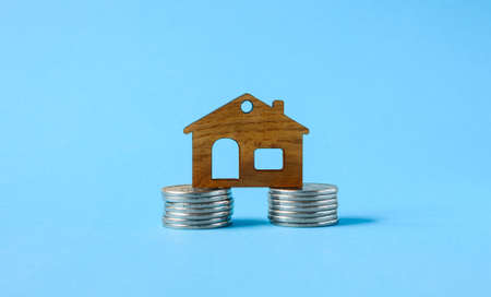 A small wooden house on a foundation of coins on a blue background.の写真素材