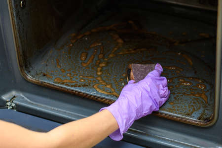 Close-up. Home cleaning concept. A woman's hand washes with a sponge on a dirty oven. Selective focus on handの写真素材