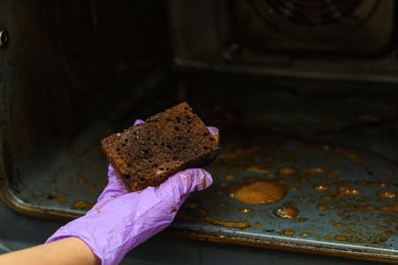 A woman's hand shows a very dirty sponge after cleaning the oven. Detergent efficiency concept. Selective focus on the sponge.の写真素材