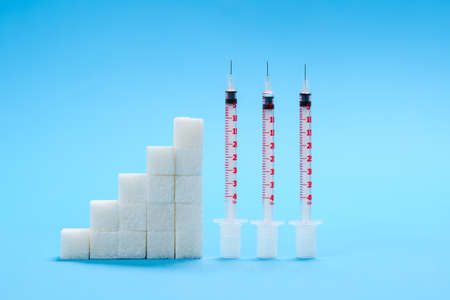 Sugar cubes in the form of a growing graph and several insulin syringes stand against a blue background. Diabetes development conceptの写真素材