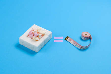 Sweets and measuring tape on a blue background. The concept of obesity from the frequent consumption...