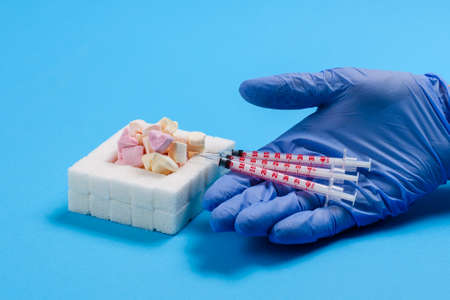 Several syringes for a diabetic in the doctor's hand next to sugar and sweets on a blue background. The concept of calling for the rejection of sweets.の写真素材