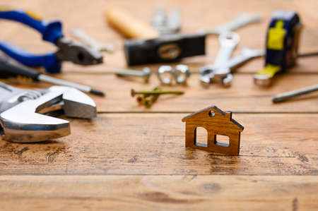 Small figurine of a house on the background of construction tools on a wooden table. House construction and renovation concept. Selective focus on a small house.の写真素材