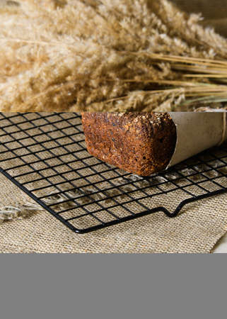 A hot loaf of rye bread on a metal stand against a background of dry grass. Focus on a loaf of bread, vertical format.の写真素材