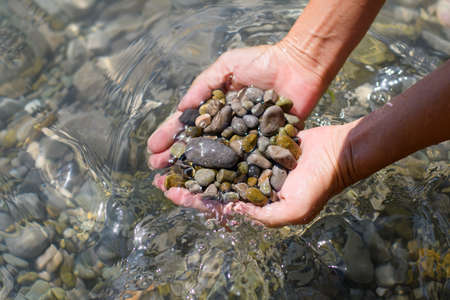 A lot of wet pebbles in female hands in sea water. Selective focus on the pebbles.の写真素材