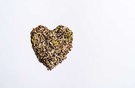 A mixture of different seeds in the shape of a heart lie on a white background. View from aboveの写真素材