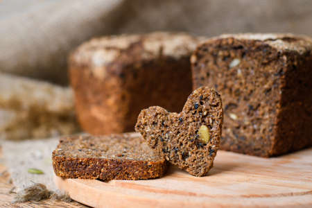 A piece of rye bread in the shape of a heart on the background of a fresh loaf. The concept of making delicious sourdough bread.の写真素材