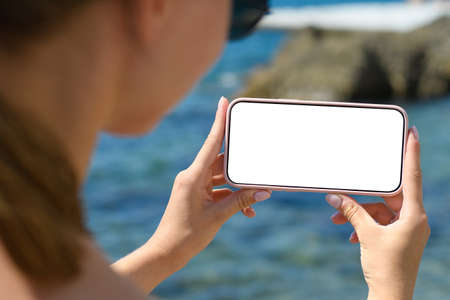The girl holds horizontally a smartphone with a blank white display on the background of the sea.の写真素材