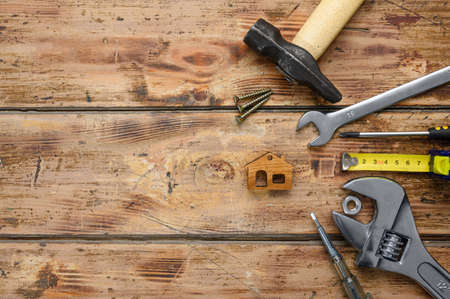 Working construction tools and a small figure of a house on an old wooden floor. Top view, empty space on the left, selective focus on the house.の写真素材