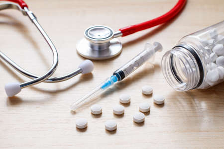 Medical care concept. Medicines, syringe, stethoscope on a wooden table. Selective focus on white tablets in the foregroundの写真素材