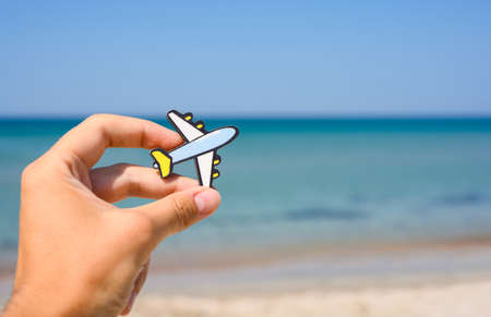 Small plane in a man's hand on the background of the beach and sea. The concept of a flight to a seaside resort.の写真素材
