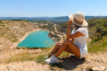 A girl sits and looks in the mountains at a blue lake in the shape of a heart. Selective focus on the girl.の写真素材