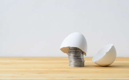 Eggshell on a stack of coins. Accumulated money protection concept. Selective focus on coins.の写真素材