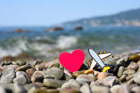 Airplane figurine and red heart on a pebble beach against the background of sea waves. Travel and sea vacation concept.の写真素材