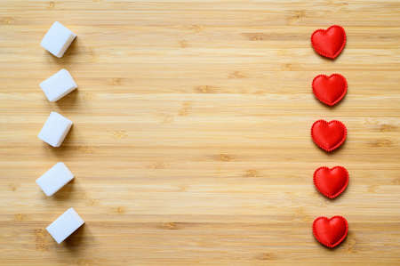 Sugar cubes and hearts on a wooden board. There is an empty space in the center. Diabetes protection...