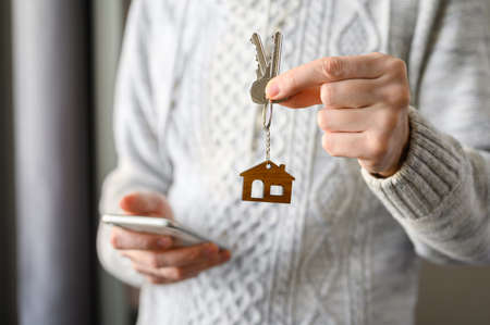 A man with a smartphone holds the keys to the house. The concept of buying or online booking accommodation. Selective focus on house keys.の写真素材