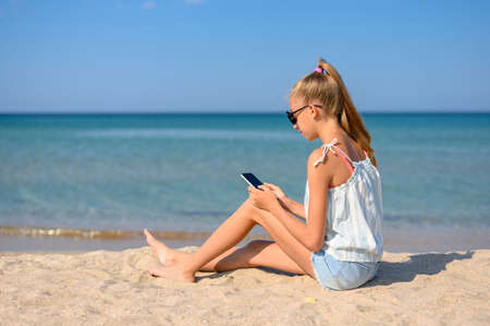 Girl sitting on the beach with a smartphone against the background of the sea.の写真素材