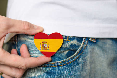 Resident of Spain. Wooden badge with Spain flag in the shape of a heart in a man's hand.の写真素材