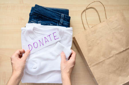 Women's hands collect children's clothes for donations. Top view, selective focus on clothes.