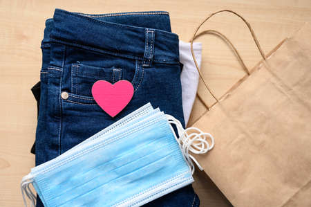 Concept for donations and assistance during the coronavirus pandemic. A red heart rests on a stack of clothing and a set of medical protective masks for donations.の写真素材