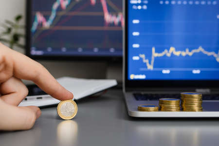 Euro coin in a man's hand against the background of increasing graphs on a computer. The concept of successful development and profit growth. Selective focus on the coin.の写真素材