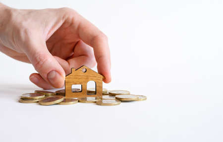 A man's hand puts a small wooden house on a pile of coins. Real estate purchase concept.Selective focus on the house.の写真素材