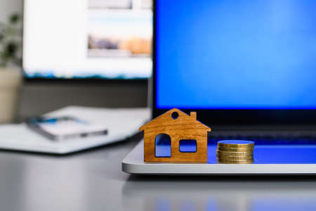 A figurine of a wooden house and some coins on the edge of a laptop. The concept of finding a profitable rental or purchase of housing. Selective focus on the house.の写真素材