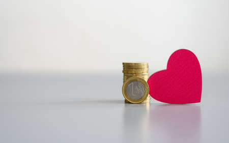 Euro coin next to a heart on a gray background. Money donation concept. Selective focus on the coin.の写真素材