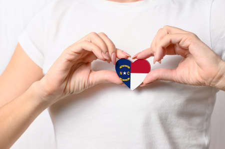 Flag of the State of North Carolina in the shape of a heart in the hands of a girl. Love North Carolina. The concept of patriotismの写真素材